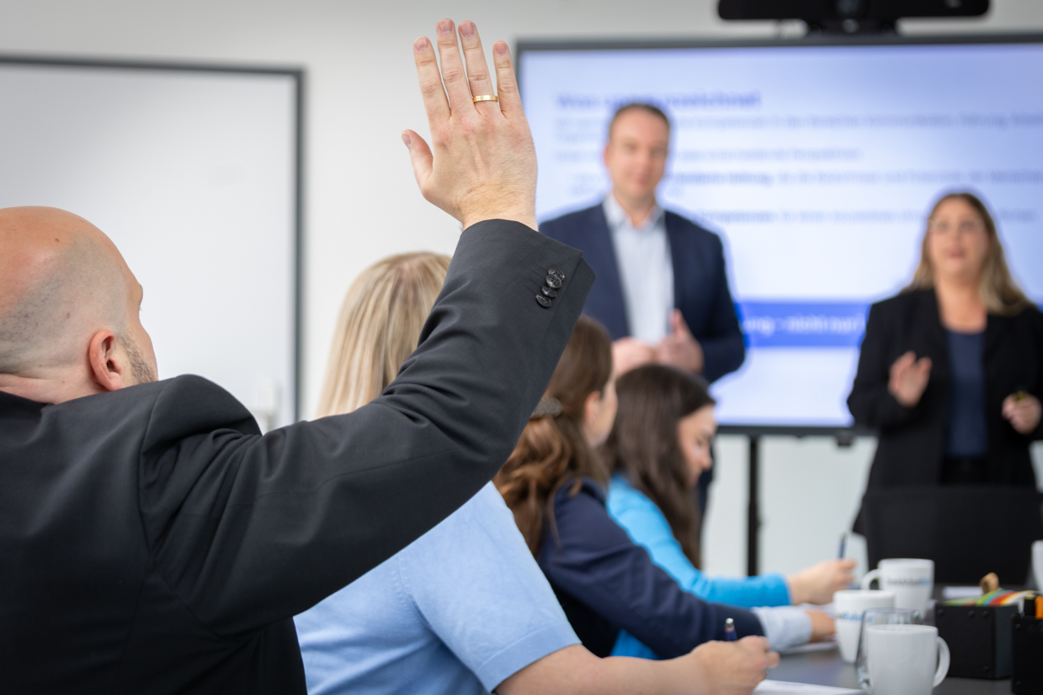 Teilnehmer hebt die Hand für eine Frage während der Präsentation